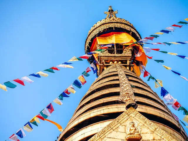 The image shows a Buddhist stupa in Kathmandu, Nepal, with colorful prayer flags fluttering around...