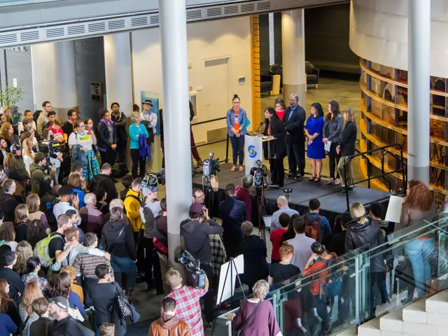 The image shows a group of people standing in front of a crowd of people, some of whom are holding...