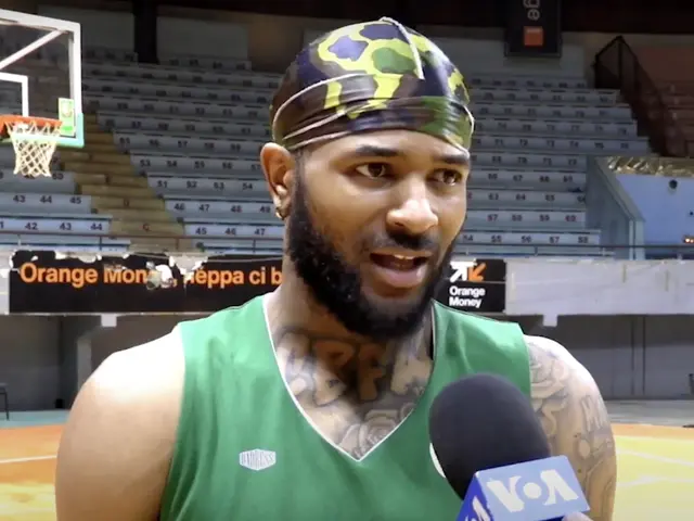 The image shows a man in a green tank top holding a microphone, standing in front of a basketball...