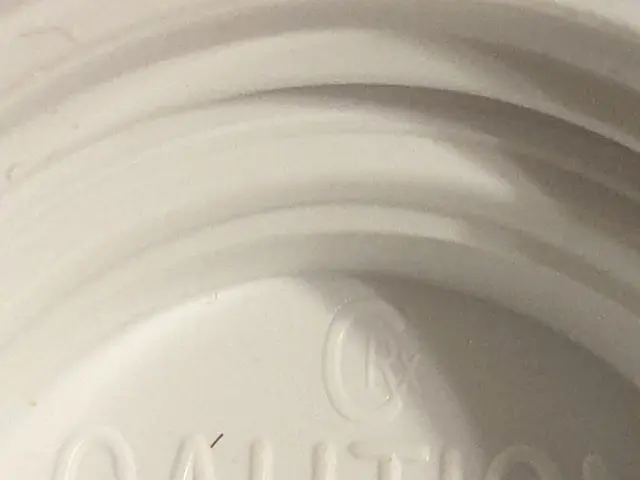 The image shows a small brown tick sitting on top of a white cup with the words "Caution Not Child...