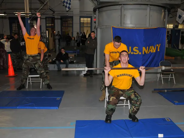 The image shows a group of men in yellow shirts and camouflage pants doing squats with a barbell in...