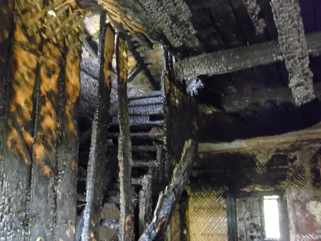 The image shows the interior of a building that has been destroyed by fire, with wooden beams and a...