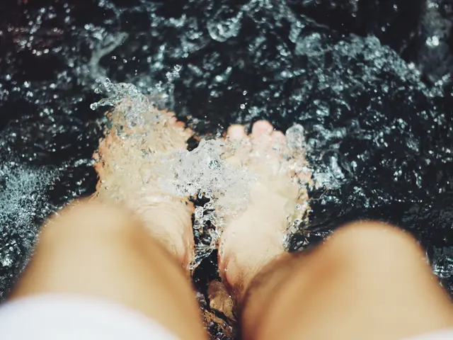 The image shows a person standing in a hot tub with their feet in the water, surrounded by a black...