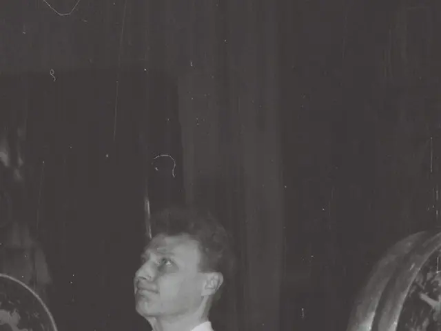 The image shows a man lifting a barbell in a gym, with a wall in the background. He is wearing a...