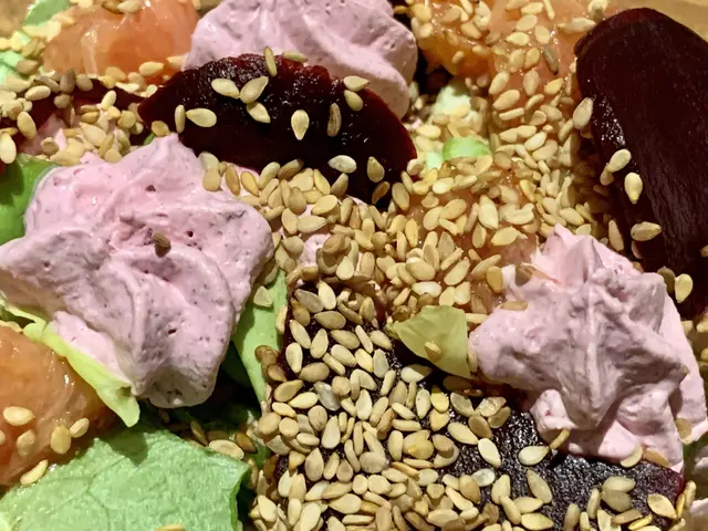 The image shows a close up of a salad with sesame seeds on top of it. The salad is composed of a...