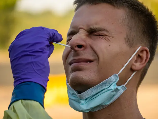 The image shows a man wearing a face mask and purple gloves, holding a syringe in his hand, with a...