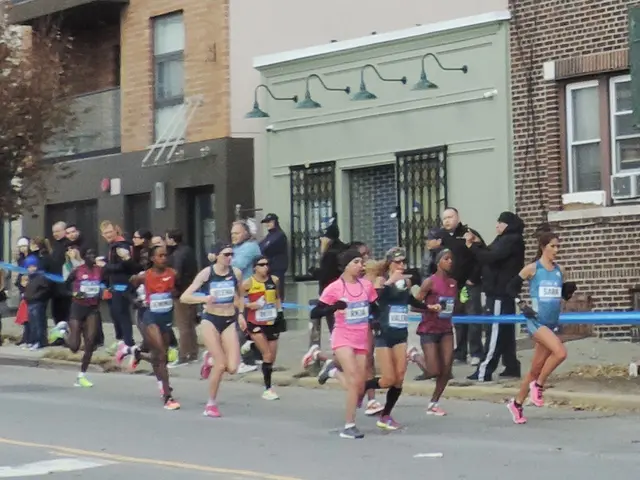 The image shows a group of people running in a marathon on a road surrounded by buildings with...