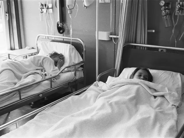 The image shows two people laying in hospital beds next to each other, covered with blankets and...