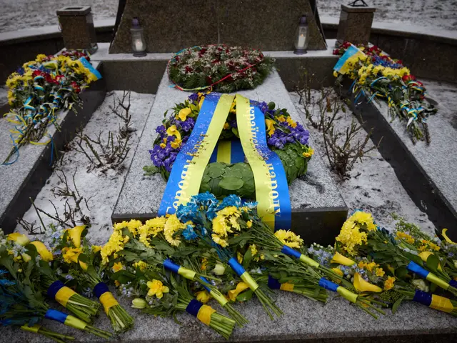The image shows a memorial in Kiev, Ukraine, with a wreath of flowers placed on the grave of a man...