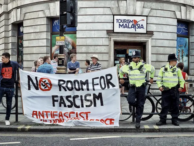 The image shows a group of people standing on the footpath, some of them holding a banner that...