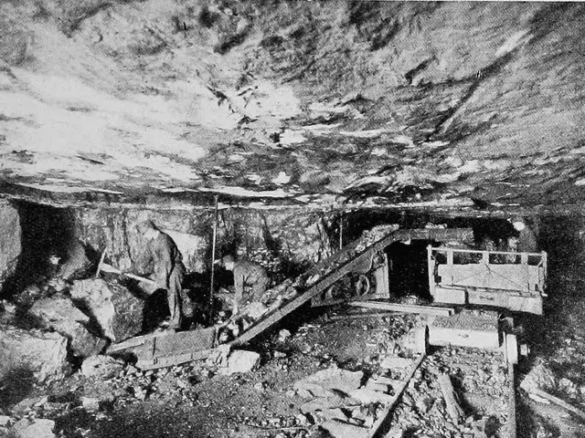 The image shows a black and white photo of a mineshaft with a few people standing in it, surrounded...